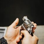 Detailed shot of hands inspecting a silver revolver in a dimly lit setting.