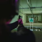 An individual aiming at a target in an indoor shooting range, seen from behind.