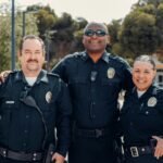 Three police officers in uniform smiling together outdoors, symbolizing community and law enforcement.