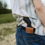 A young man outdoors with a gun tucked into his belt, captured from behind.